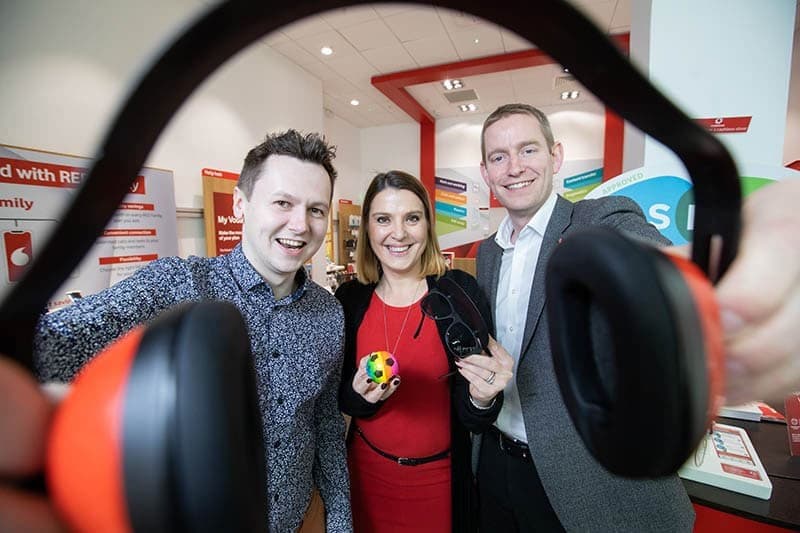 Three people holding noise cancelling headphones in a Vodafone store.