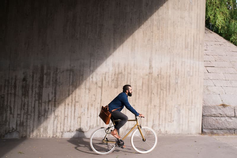 A man cycling a bicycle under a bridge.