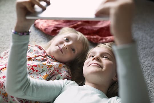 Kids taking selfie on floor with tablet at home