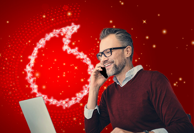 Man on phone looking at computer with Christmas lighting behind him
