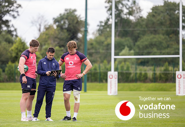 Two rugby players talking to coach and looking at tablet on pitch
