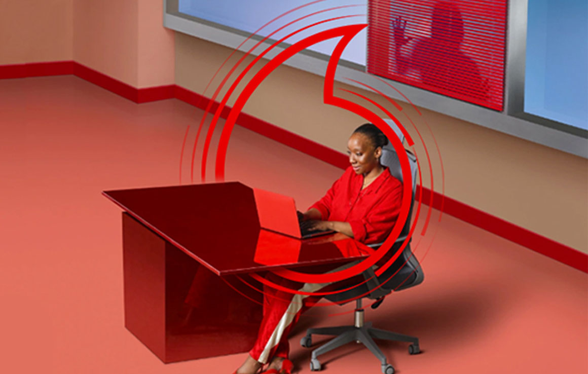 Image of working at desk in a open room with a hacker trying to steal information behind her