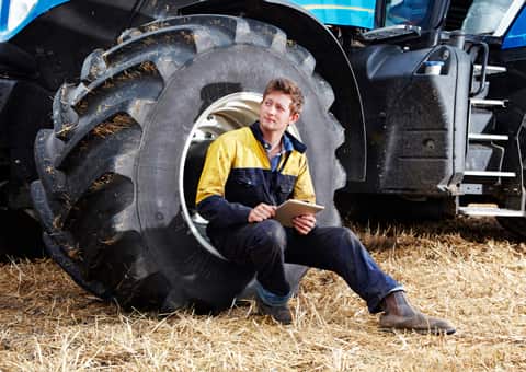 Farmer sitting on tracker wheel with tablet in hand