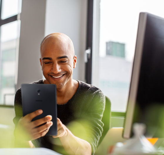 A smiling man looking at a tablet in an office.