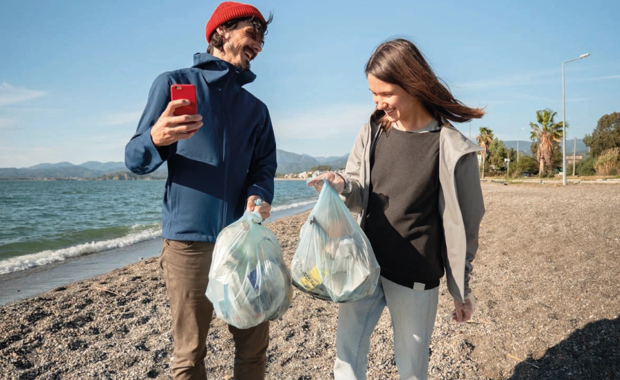 A man and a woman collecting rubbish on a beach.