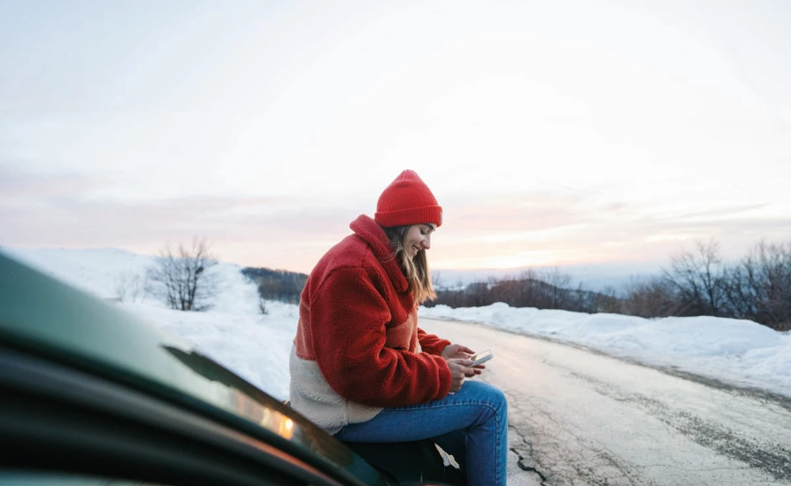 A smiling girl outside in the snow, texting on her phone.