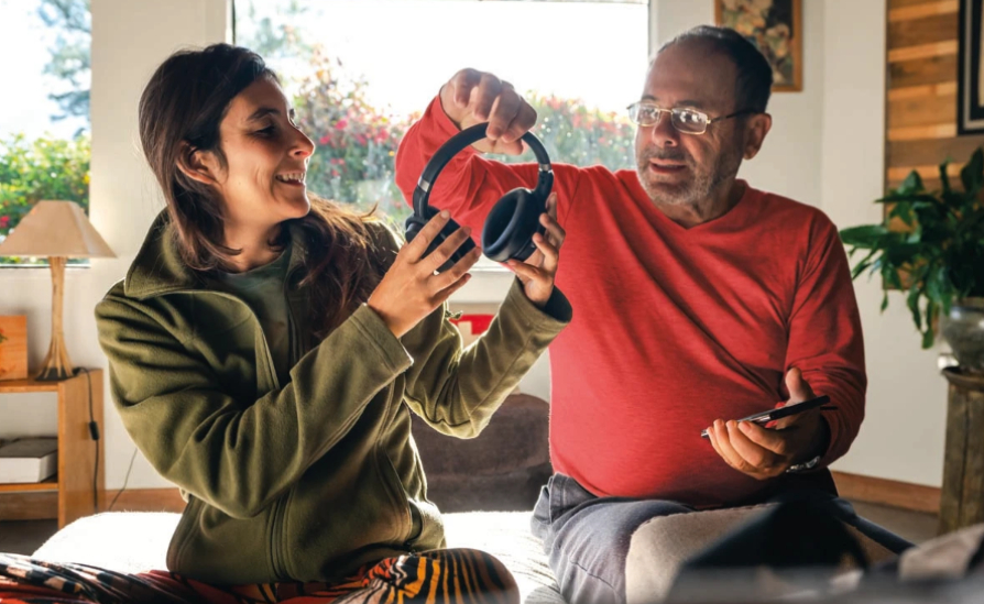 A man and woman in a home, smiling and holding the same pair of headphones.