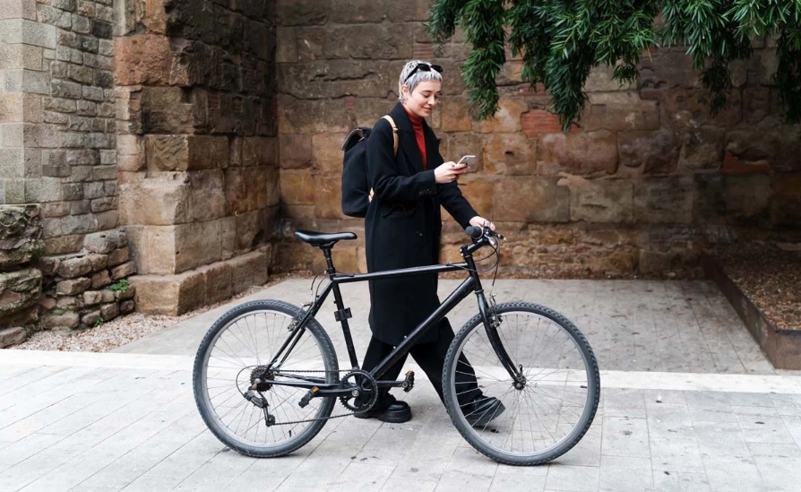 A stylish woman pushing a bicycle and looking at her phone.