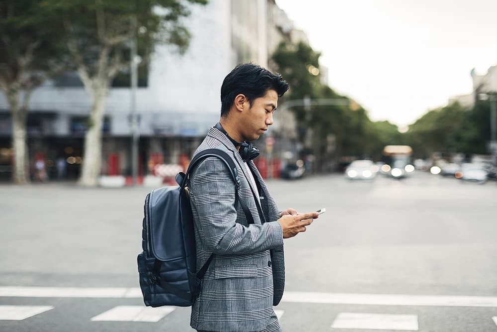 Man with backpack crossing the road looking at his phone.