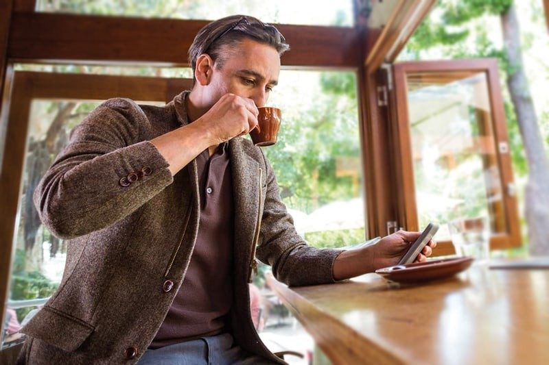 Man drinking coffee and looking at phone.